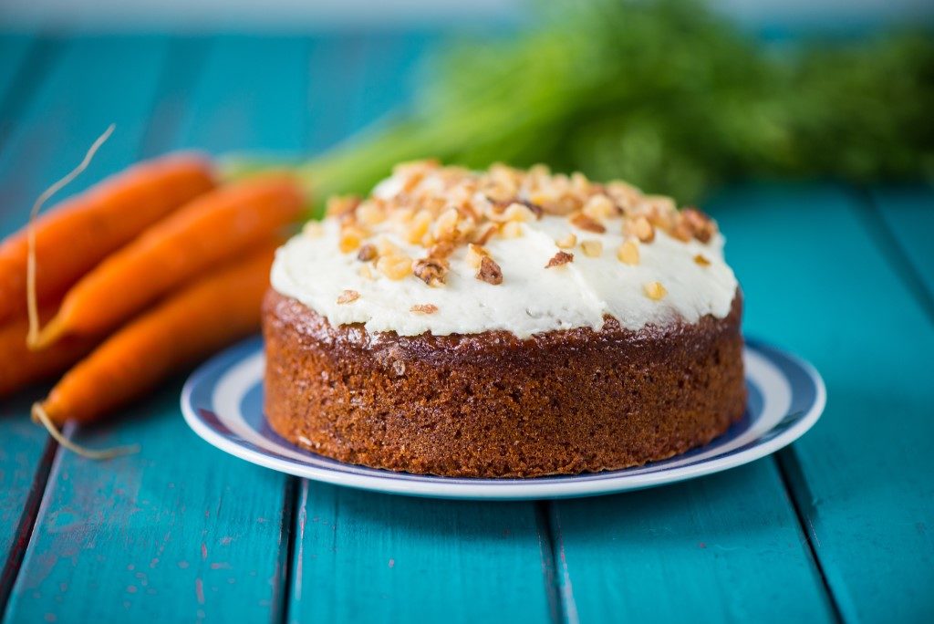 Carrot cake sat on plate on blue table with fresh carrots next to it